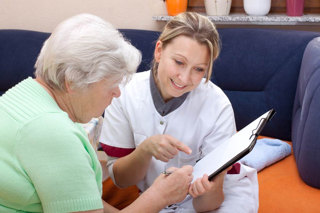 Seniorin und Pflegerin sitzen beieinander, Daten werden notiert